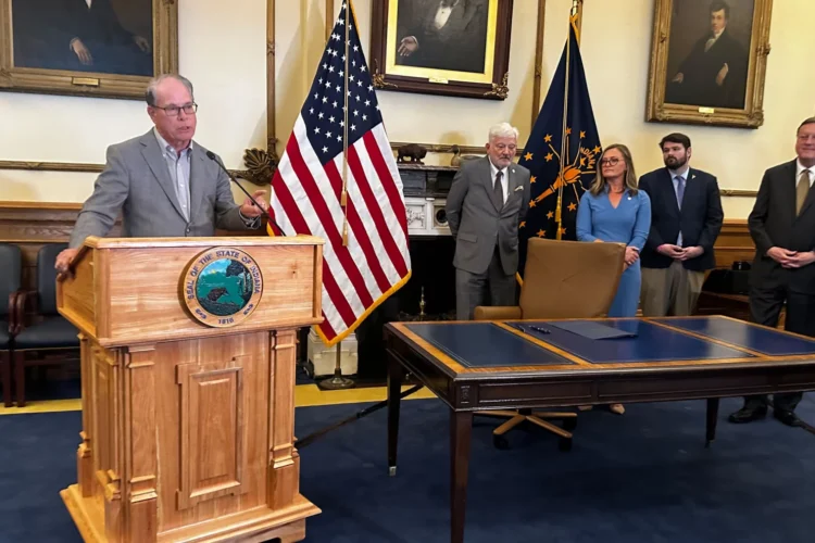 Governor Mike Braun stands at a podium, talking about the new law. He is surrounded by officials waiting to talk about the law.