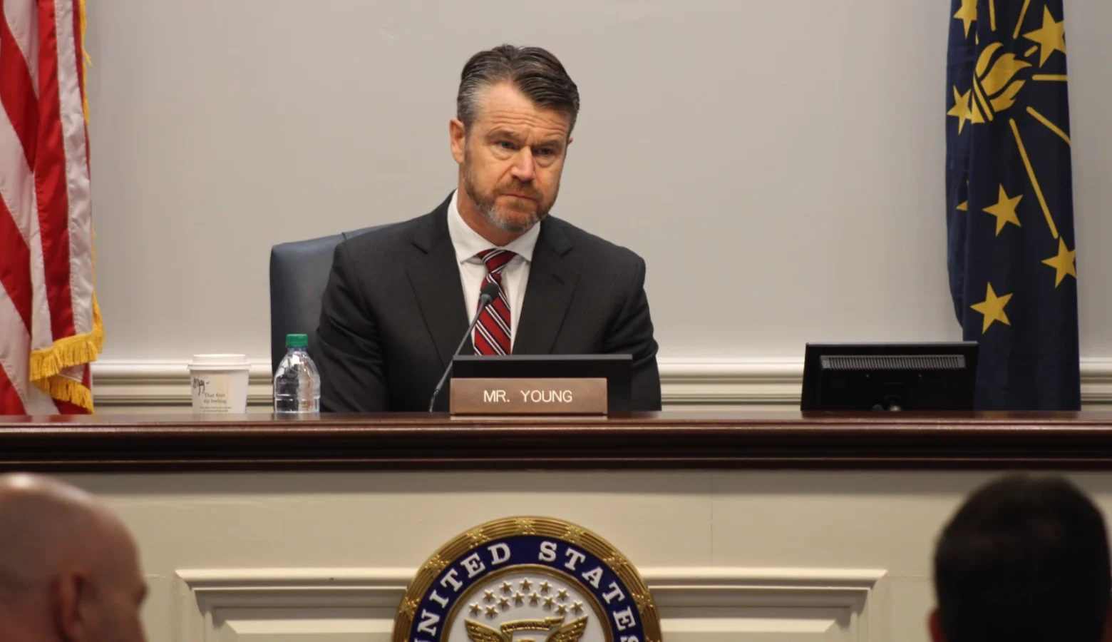 U.S. Senator Todd Young sits at a desk, in front of a microphone, answering questions.
