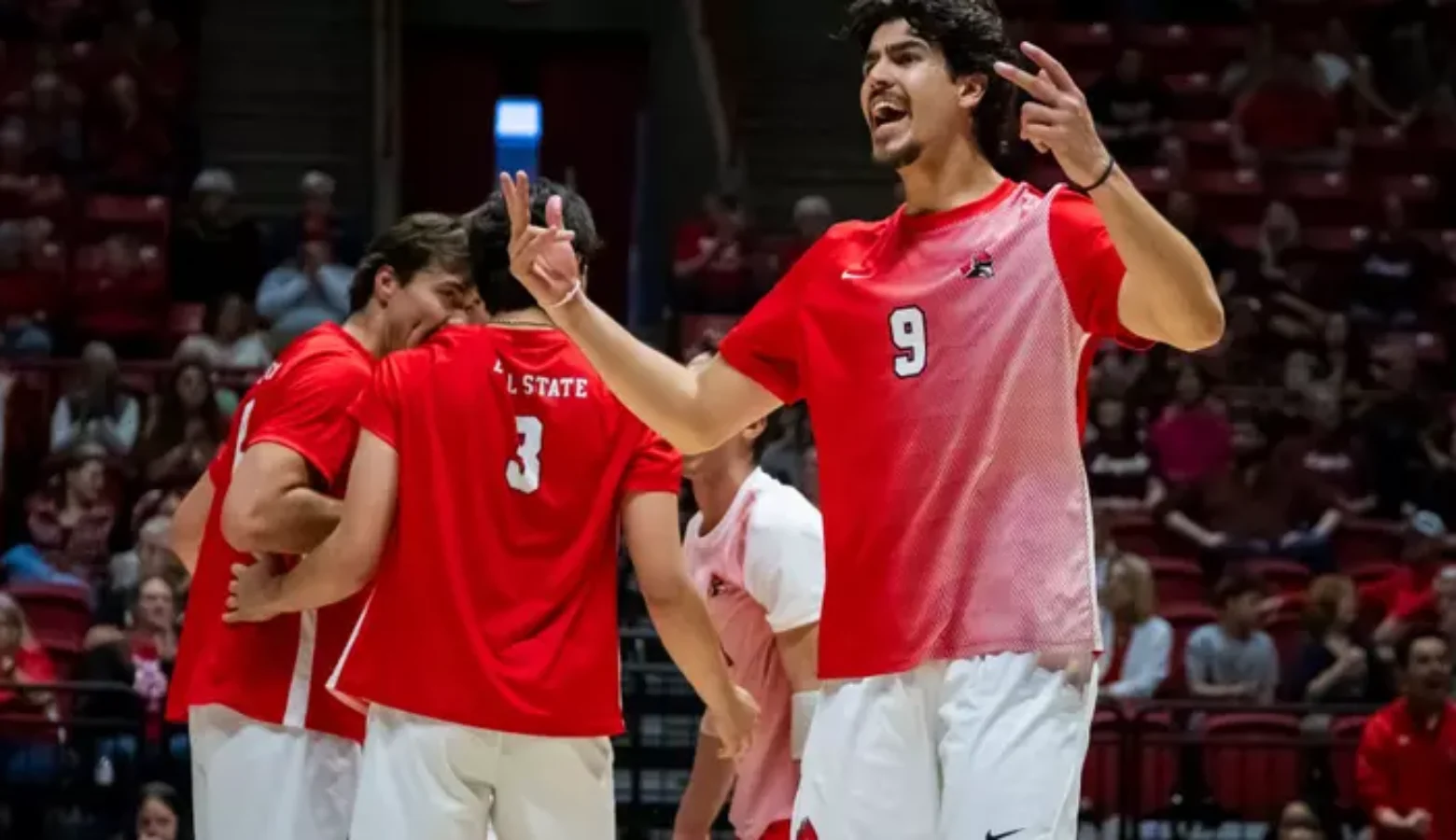 Ball State men's volleyball players celebrate a point. They are dressed in red jerseys and white pants.