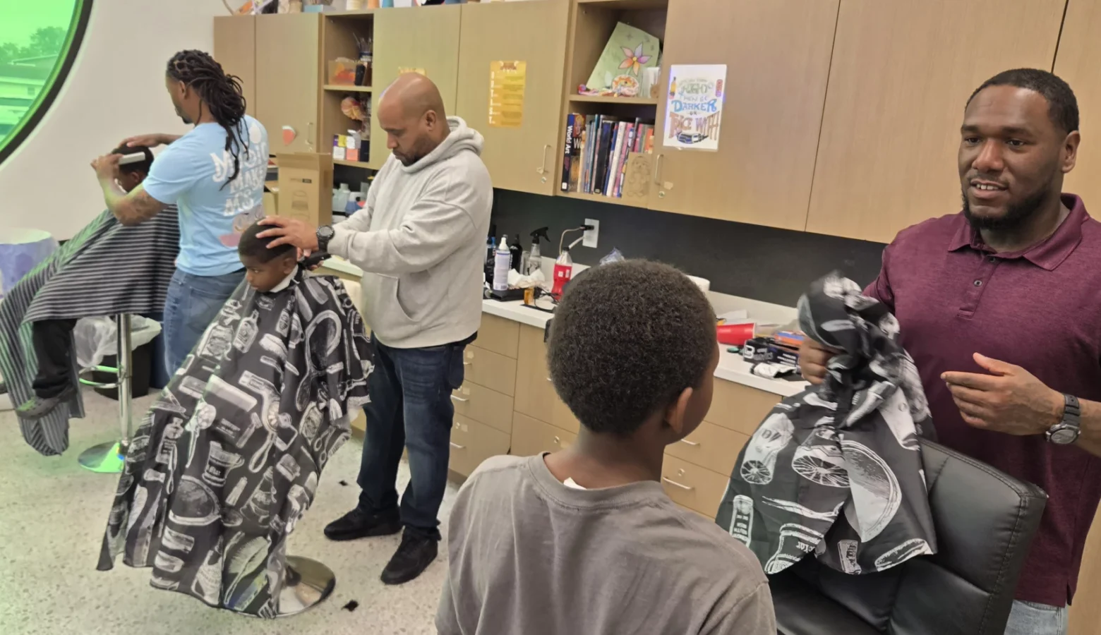 A photograph in a barbershop with three adult barbers giving three boys haircuts.