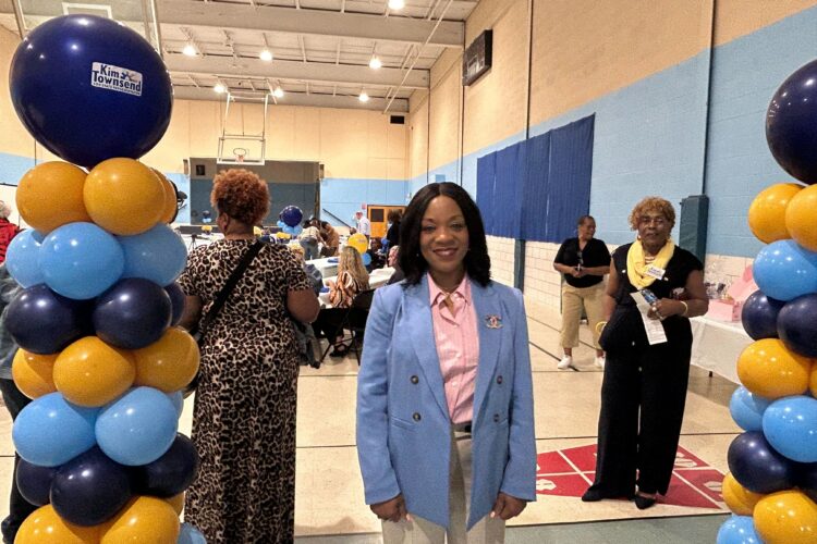 A woman in a suit stands between two multi-colored balloon arches