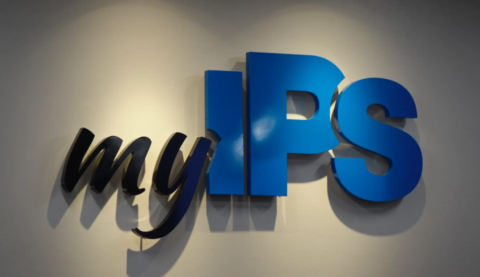 A photo of the "my IPS" logo in blue and black metal lettering hanging on a gray wall.
