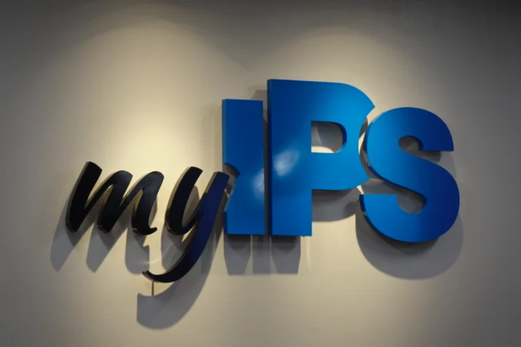 A photo of the "my IPS" logo in blue and black metal lettering hanging on a gray wall.