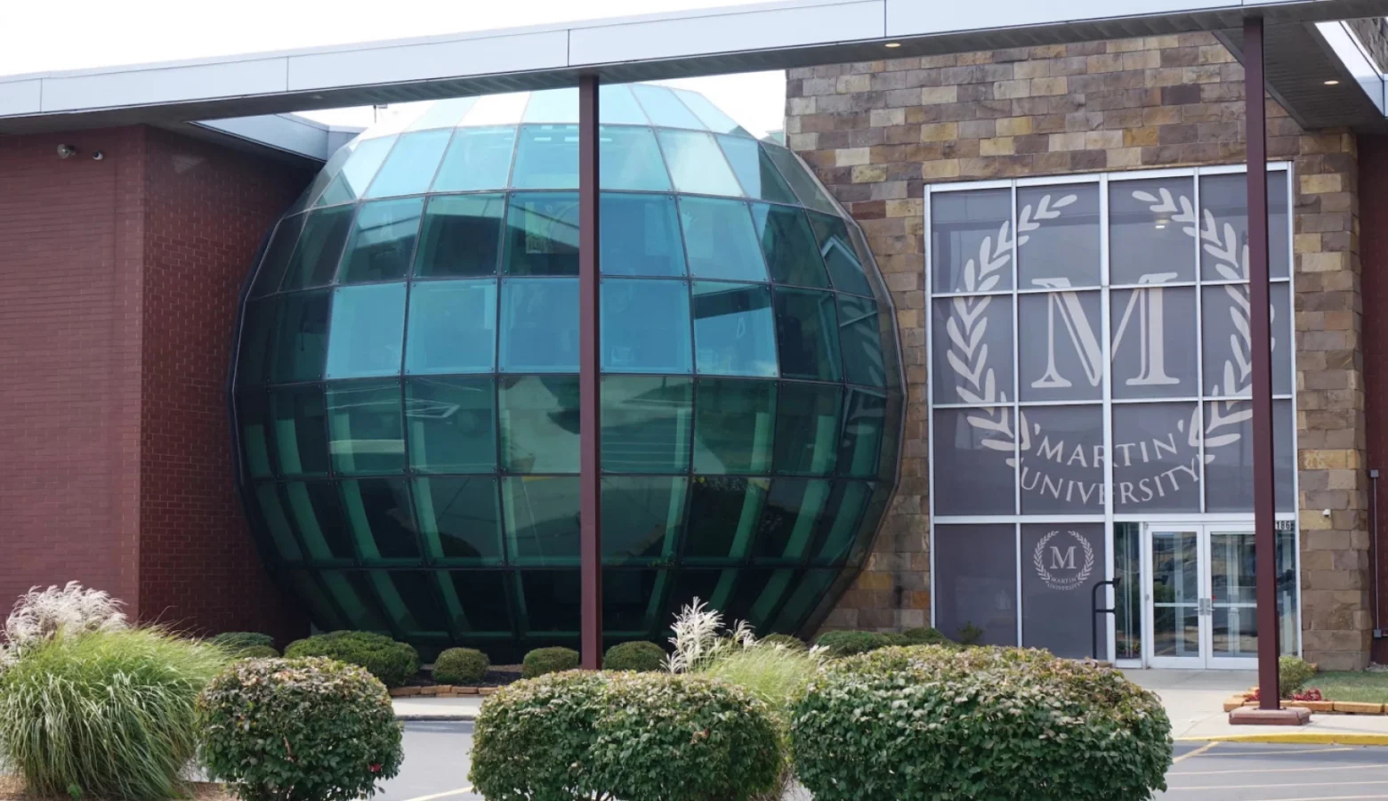 An exterior view of the former Martin University's main entrance featuring a large glass globe to the left of the front doors, and the Martin University logo behind glass above the front doors.
