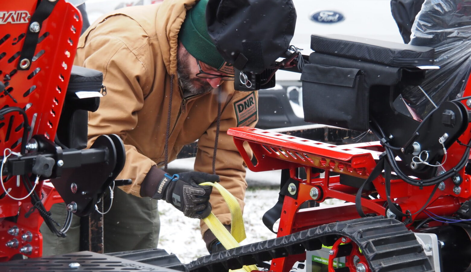 A man straps several black and red specialized track wheelchairs to a trailer.