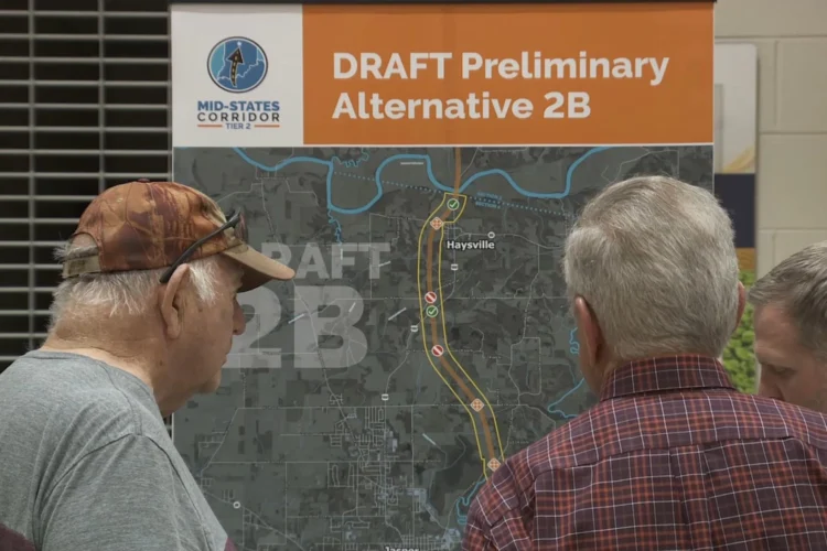 Two older men stand in front of a map showing a preliminary map for a road corridor