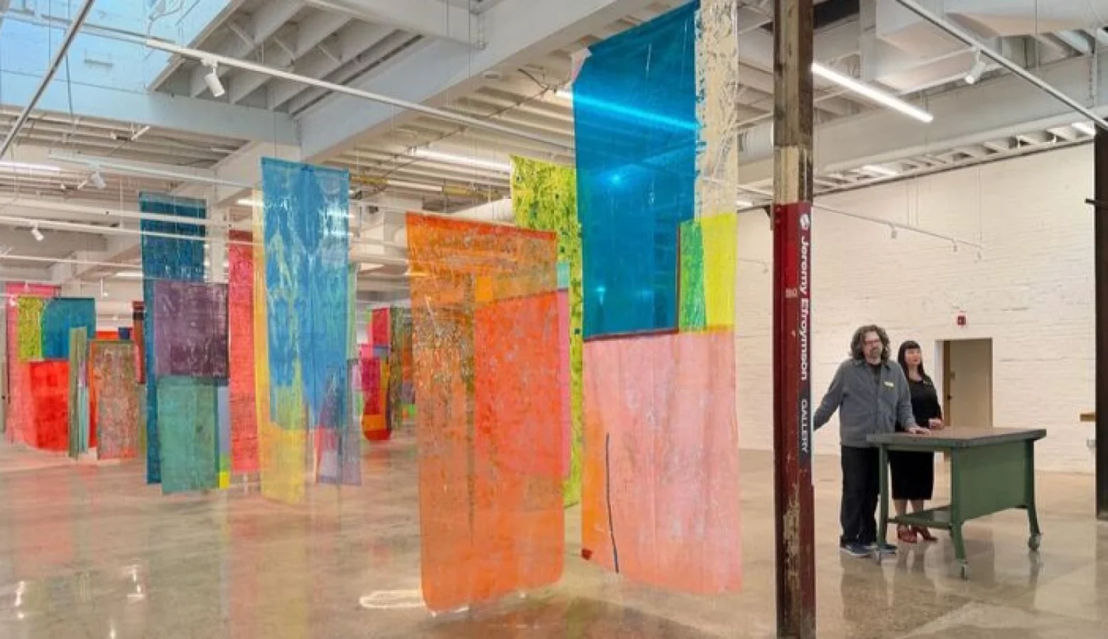 Colorful fabrics hang from the ceiling of the inside of a very tall building.