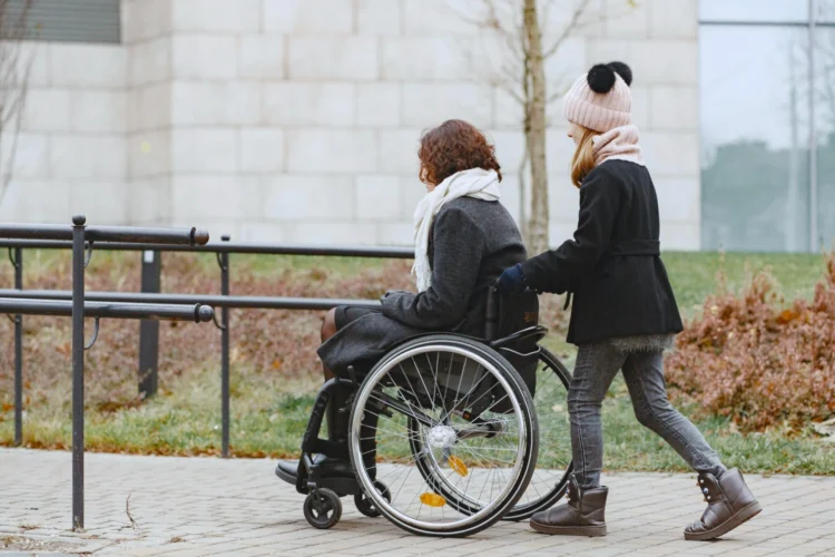 A woman pushes a woman sitting in a wheelchair up an accessible ramp.