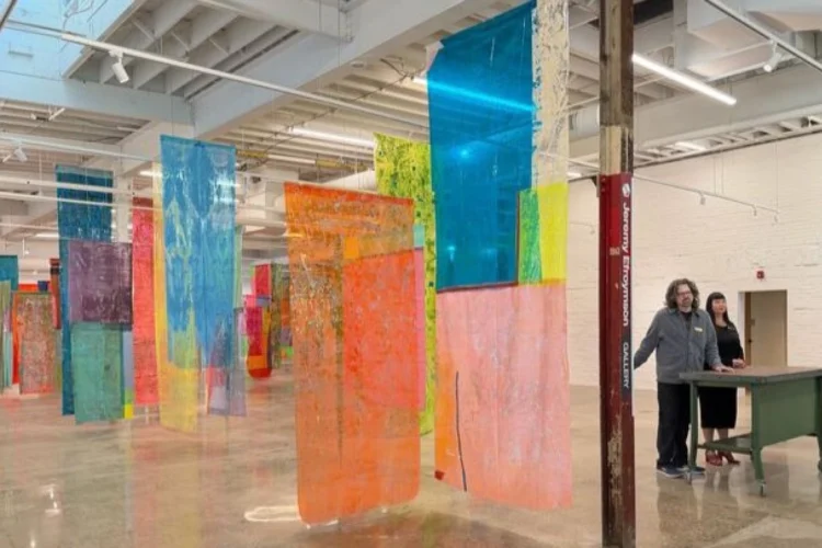Colorful fabrics hang from the ceiling of the inside of a very tall building.
