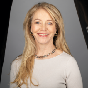 Elizabeth "Liza" Yntema stands smiling for a portrait. She has long blonde hair and is wearing a long sleeve top and a necklace.