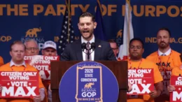 Max Engling speaking to delegates Saturday, June 20, 2026 at the Republican Party convention in Fort Wayne. He is standing behind a podium with a GOP State Convention logo within a blue circle on the front of the podium. He is flanked by supporters holding signs saying "Citizen Only Voting -- Vote Max"