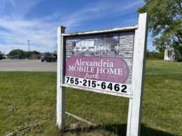 An old wooden sign with a faded image and the words "Alexandria Mobile Home Park"