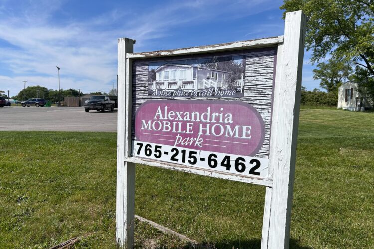 An old wooden sign with a faded image and the words "Alexandria Mobile Home Park"