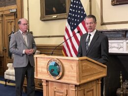 Commerce Secretary David Adams stands at a podium in the Indiana governor's office. Next to him is Governor Mike Braun.