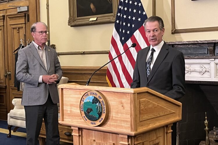 Commerce Secretary David Adams stands at a podium in the Indiana governor's office. Next to him is Governor Mike Braun.