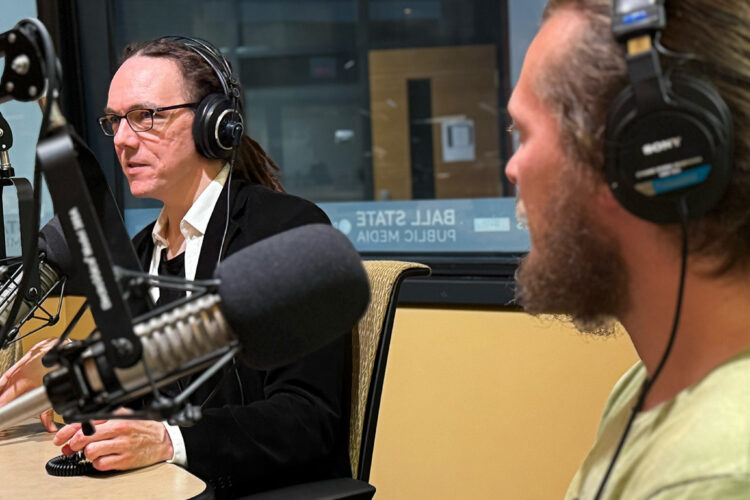 Graham Watson and Braiden Robinson sit in a radio studio wearing headphones. Graham is talking into a microphone.