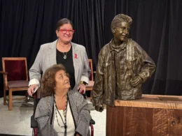 A bronze sculpture of Ryan White was unveiled at the Indiana Memorial Union. White's mom, Jeanne White-Ginder, and his sister, Andrea White, stand next to it. The bronze statue is from the waist up and is placed on a wooden pedestal.