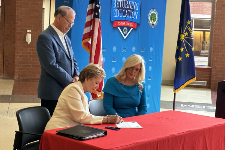 U.S. Education Secretary Linda McMahon sits to sign a state waiver on education funding. She is joined at the table by state Education Secretary Katie Jenner. Standing behind them is Indiana Gov. Mike Braun.