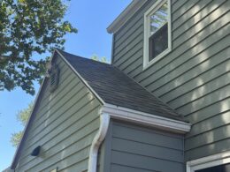 A close-up of a two-story home with green siding, gray roof, and white trim and gutters.