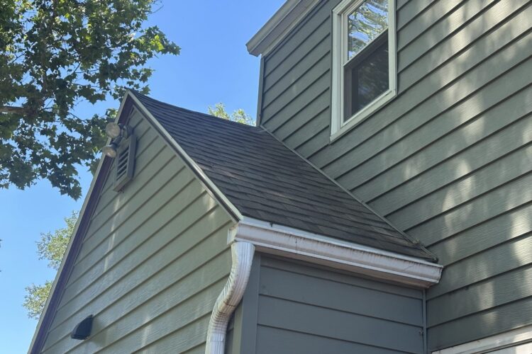 A close-up of a two-story home with green siding, gray roof, and white trim and gutters.