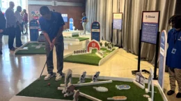 A person stands at a small mini-golf display, about to shoot a ball towards the hole.