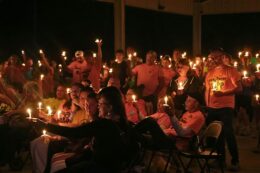 Many people stand together, wearing pink t-shirts and holding lit candles.