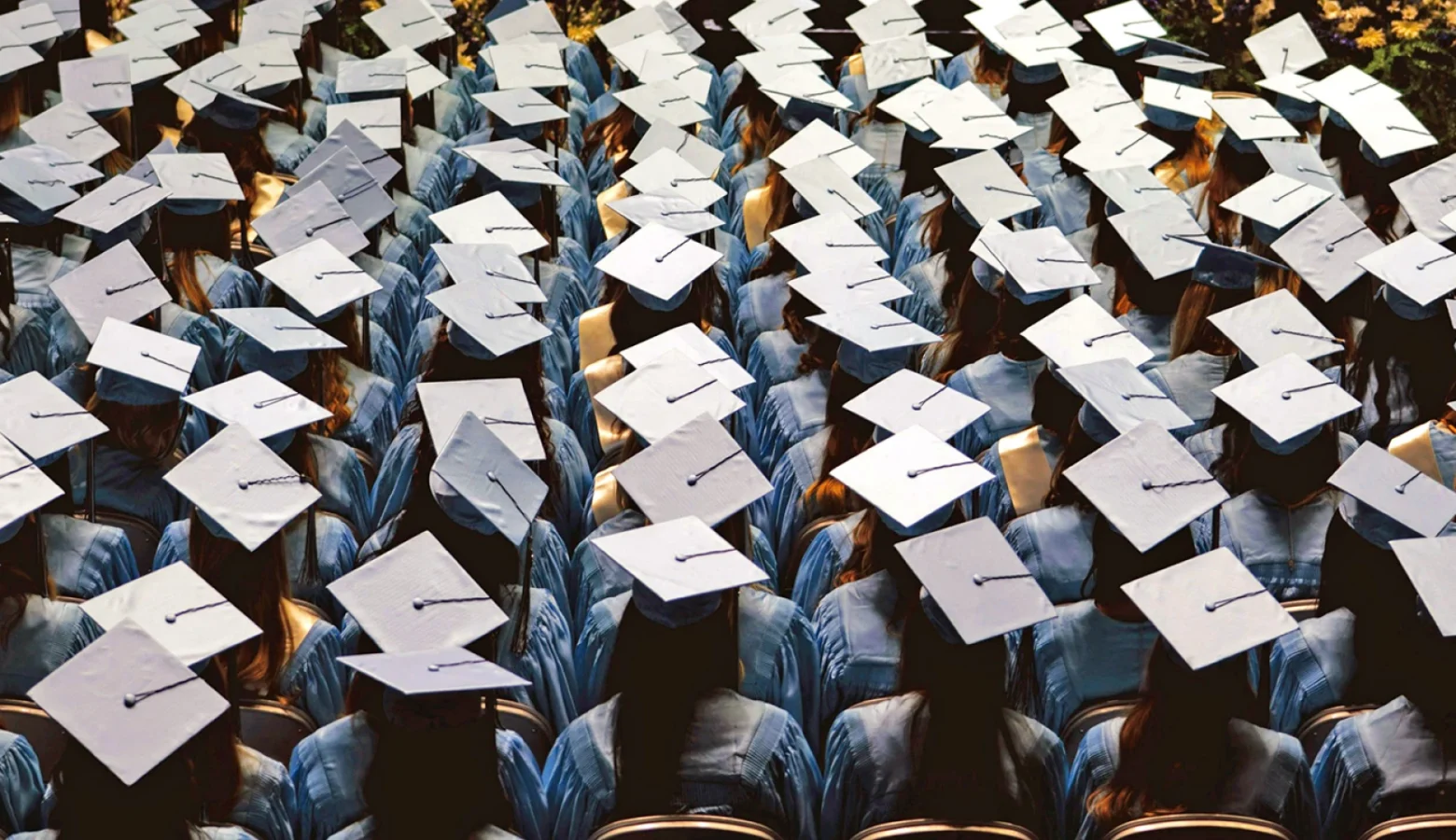 Rows and rows of mortar-board bedecked college graduation candidates are photographed from above and behind during a commencement ceremony. No faces are visable.