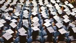 Rows and rows of mortar-board bedecked college graduation candidates are photographed from above and behind during a commencement ceremony. No faces are visable.