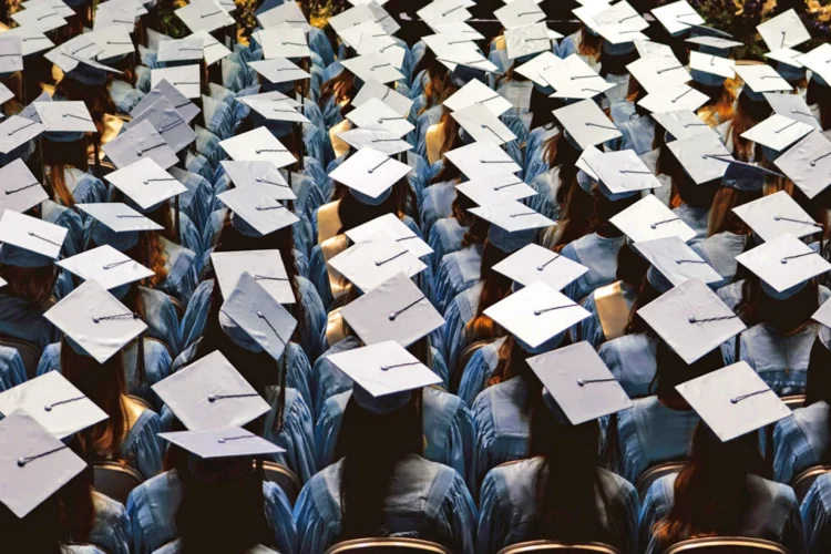 Rows and rows of mortar-board bedecked college graduation candidates are photographed from above and behind during a commencement ceremony. No faces are visable.