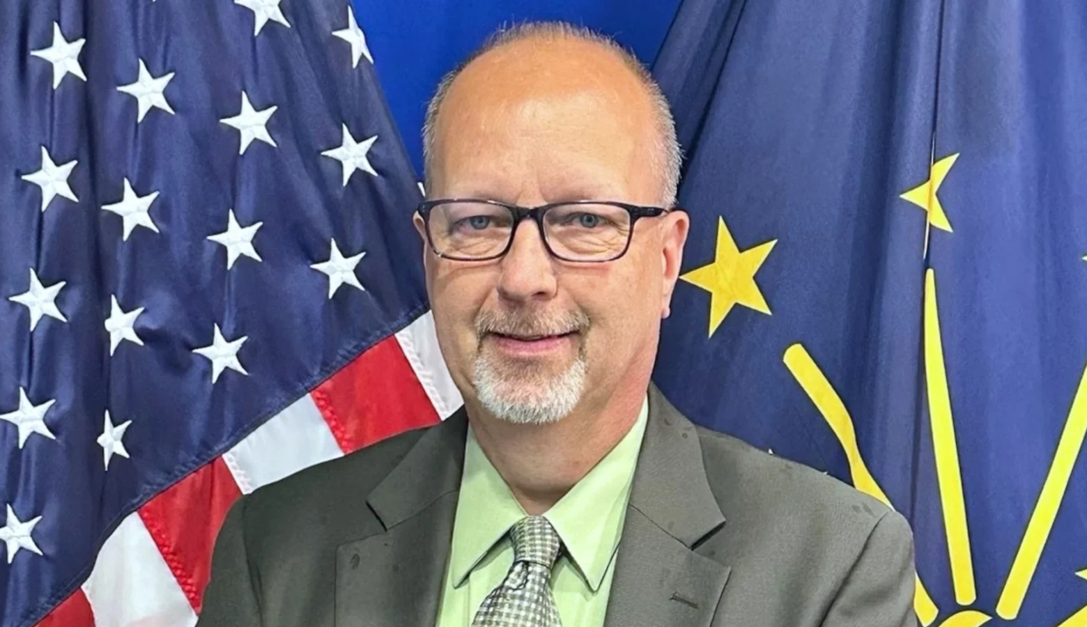 Gov. Mike Braun announced the appointment of Joby Jerrells to the Indiana Utility Regulatory Commission on Wednesday, July 22, 2026. Mr. Jerrells is photographed in a medium closeup, wearing a suit, and standing in front of American and Indiana flags.