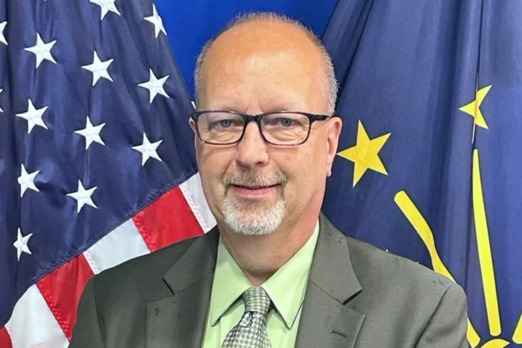 Gov. Mike Braun announced the appointment of Joby Jerrells to the Indiana Utility Regulatory Commission on Wednesday, July 22, 2026. Mr. Jerrells is photographed in a medium closeup, wearing a suit, and standing in front of American and Indiana flags.