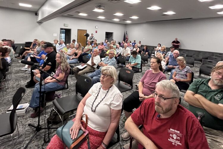 A crowd of a few dozen people sit in rows of chairs and face forward