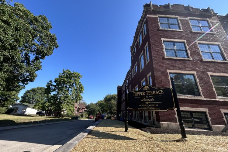 The outside of a three story brick building with a sign in front reading "Topper Terrace at Lincoln"