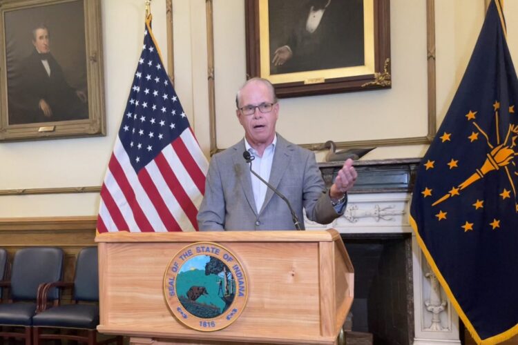 Governor Mike Braun speaks from a podium in his office, surrounded by the American and Indiana flags.