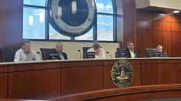 Members of the Indiana Utility Regulatory Commission listen to customers' concerns about utility rates during public meeting at Noblesville City Hall, Thursday, April 9, 2026. Five commissioners are seated at a curved bench behind wood paneling with name signs and microphones in front o them. A large Noblesville city seal is on an illuminated wall behind the commissioners.