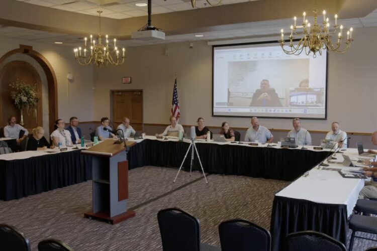 A video screenshot shows a meeting of the Natural Resources Commission, whose members are sitting around a u-shaped table formation in a conference room.