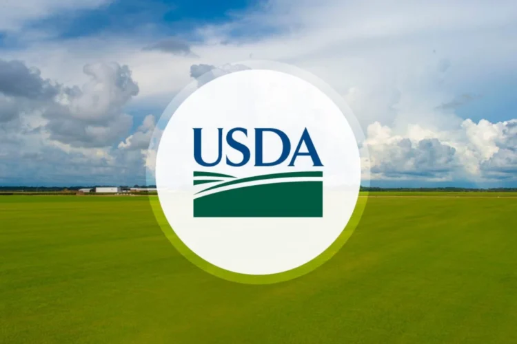 The green and blue USDA logo in a white circle superimposed over a large, green field under a cloudy sky.