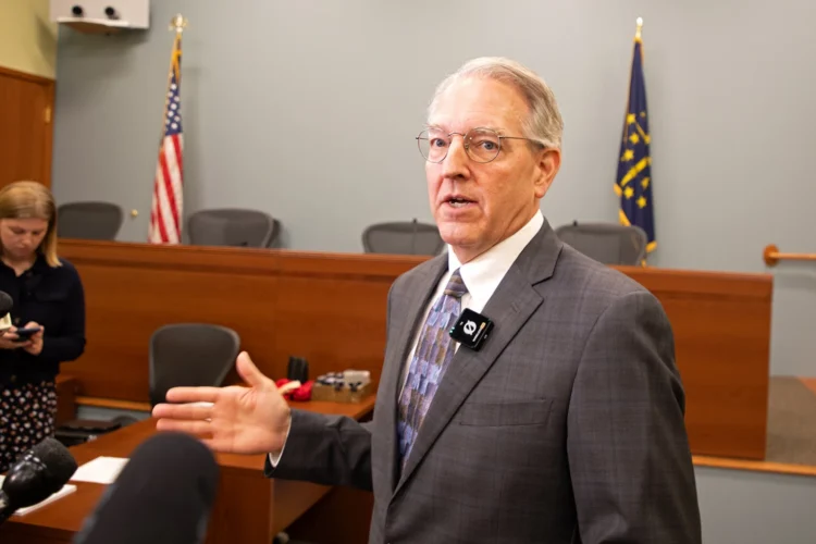 Indiana State Rep. Matt Pierce (D-Bloomington) held a press conference after the IURC’s updates on utility investigations Wednesday, July 15, 2026. He is standing while talking to reporters. He is wearing a gray suit and gesturing with his right hand. His press conference was held in a council meeting room with a panel with chairs (unoccupied) in the background, and other chairs and tables in the foreground where reporters are standing.