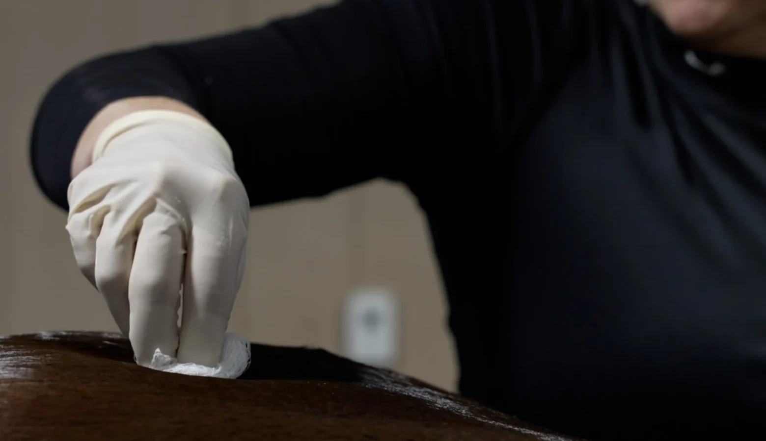 A veterinarian performing work on a horse. He is wearing a white, vinyl glove and is rubbing a preparation with gause on the top side of the horse toward its back end.