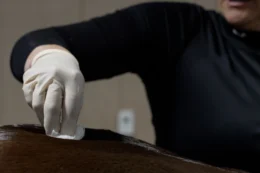 A veterinarian performing work on a horse. He is wearing a white, vinyl glove and is rubbing a preparation with gause on the top side of the horse toward its back end.