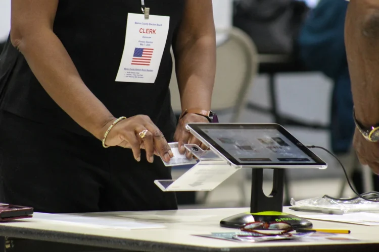 A poll worker for the Marion County Clerk's Office checks a voter's identification card during the May 2024 primary election. The worker is scanning a card that is part of a touchscreen device.