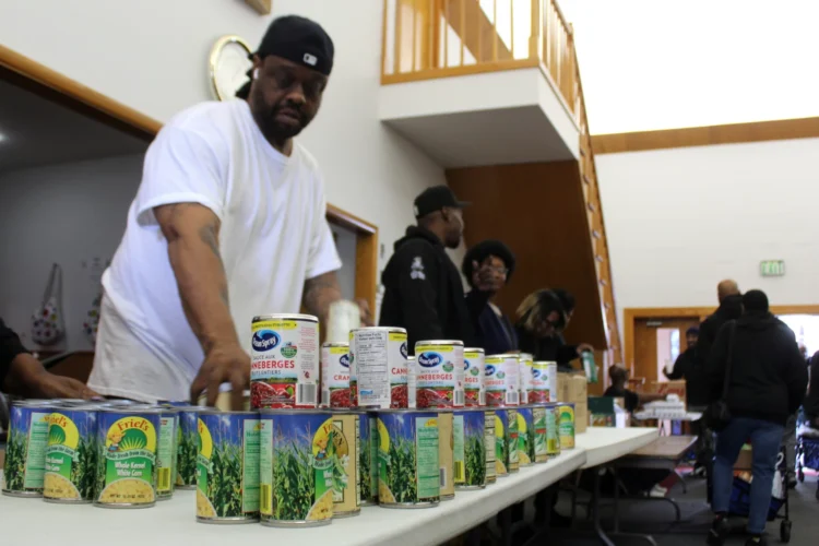 Several people stand behind folding tables, stacking canned food.