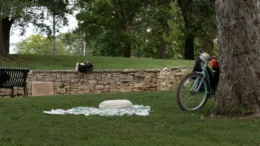 A blanket and pillow lay in the grass at a public park in Bloomington. Next to the blanket, a bicycle leans against a tree.