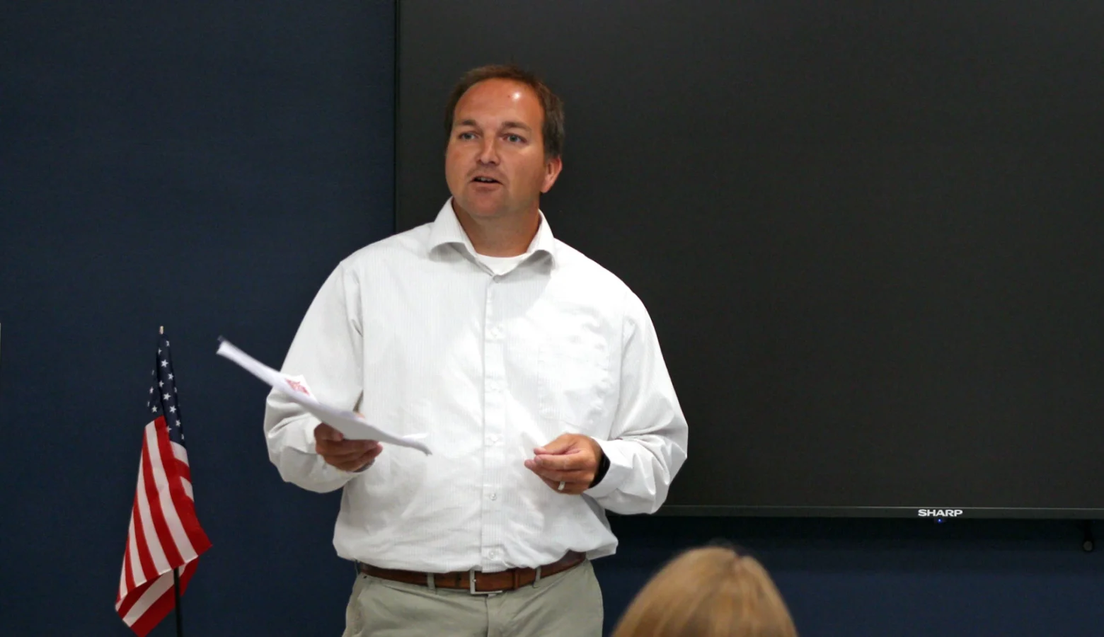 Representative J.D. Prescott stands in front of a community meeting, reading from papers in his hand.