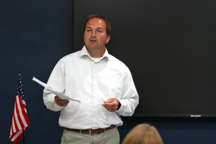 Representative J.D. Prescott stands in front of a community meeting, reading from papers in his hand.