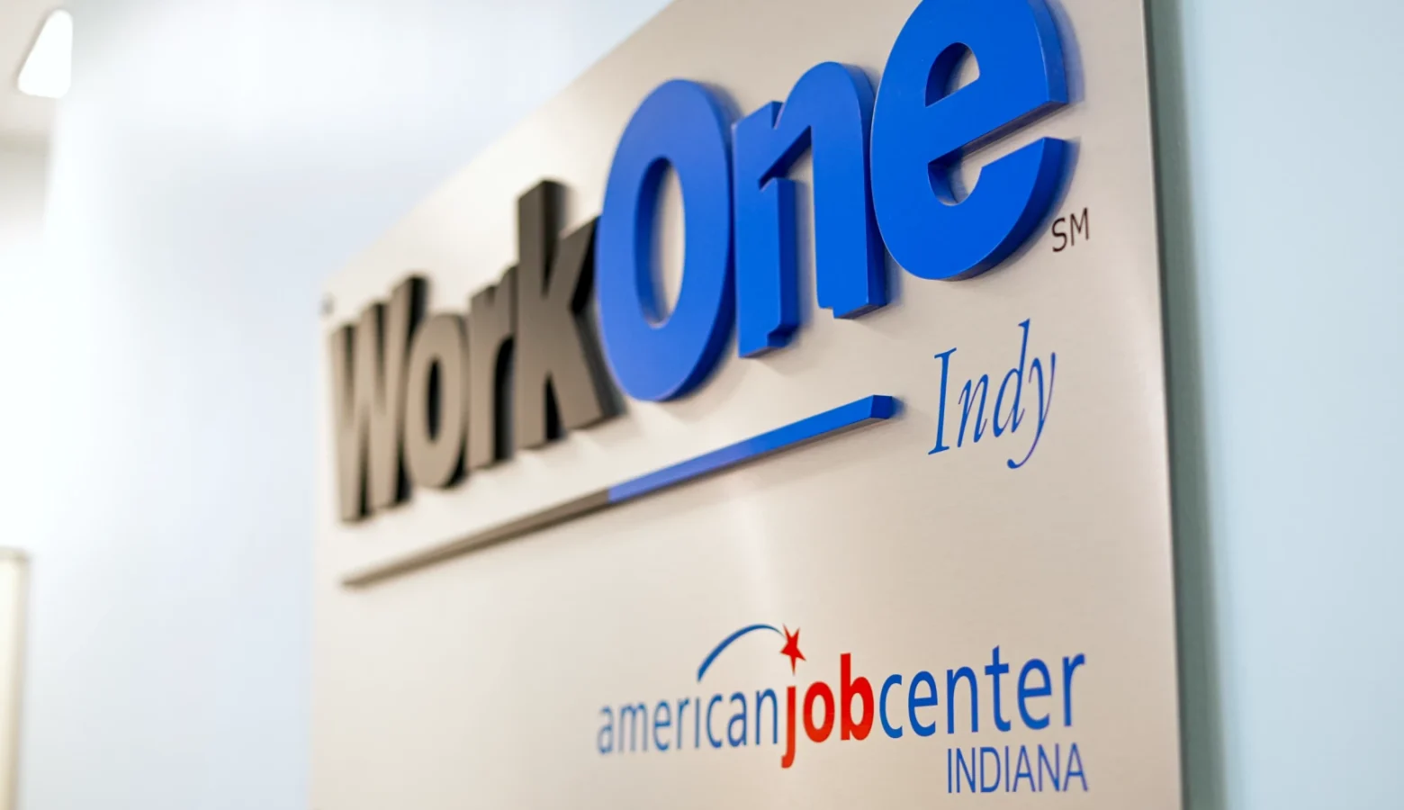A metal plaque on a wall shows the logo of WorkOne Indy.