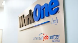 A metal plaque on a wall shows the logo of WorkOne Indy.