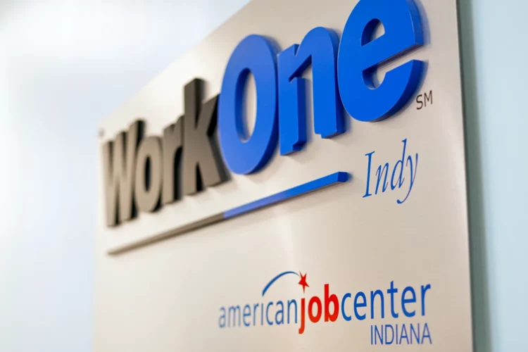 A metal plaque on a wall shows the logo of WorkOne Indy.