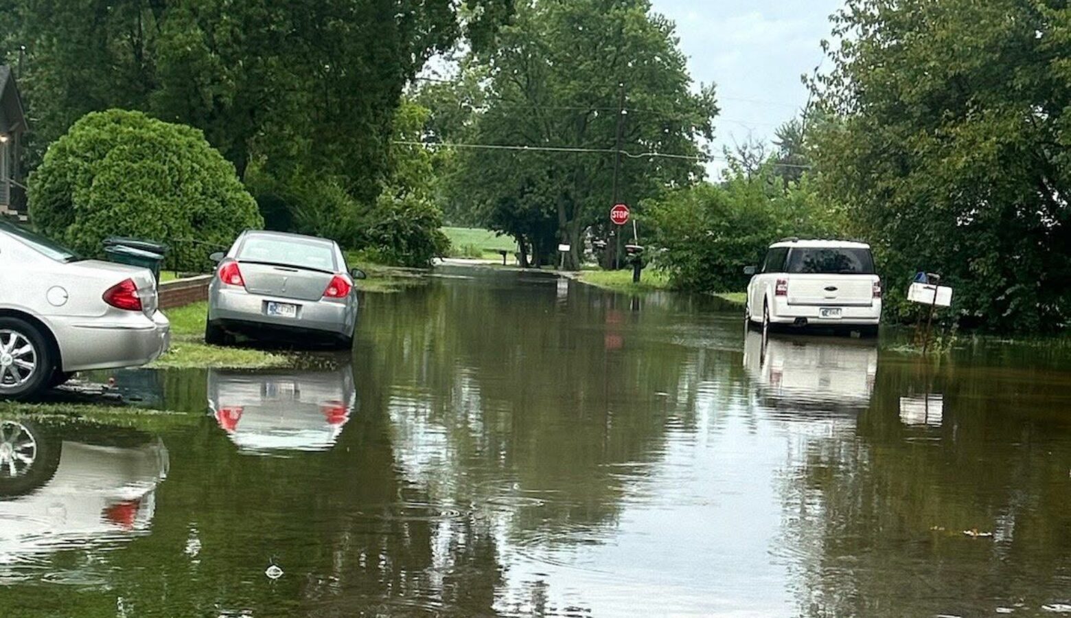 Cars park on grass surrounding a flooded street in Muncie.