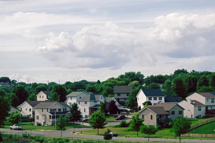 The photo is a wide exterior shot of three and four bedroom houses in a tree-filled neighborhood under cloudy skies.